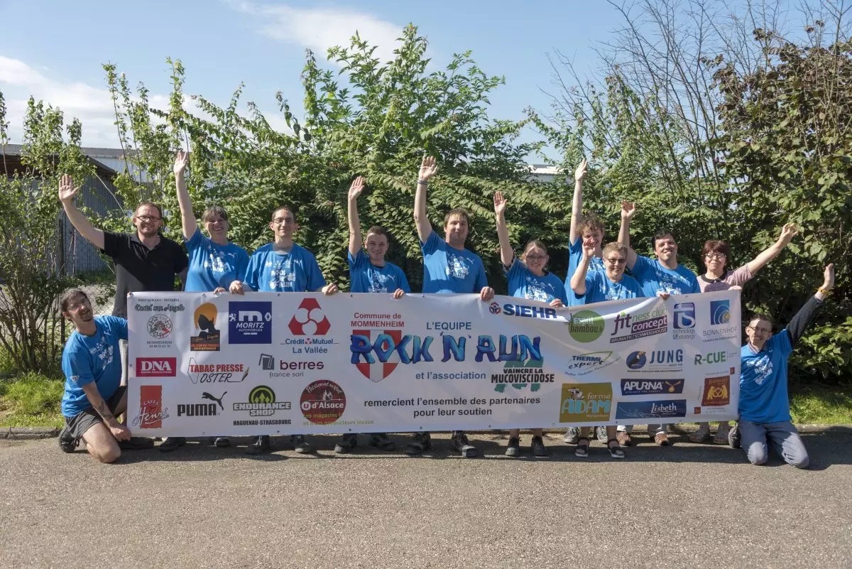 Photo de groupe des travailleurs handicapés tenant une banderole représentant les partenaires et sponsors des Ateliers